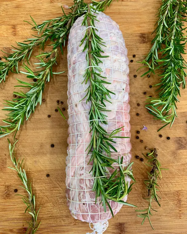 Arrosto di carne legato con la rete e un rametto di rosmarino, su un tagliere di legno