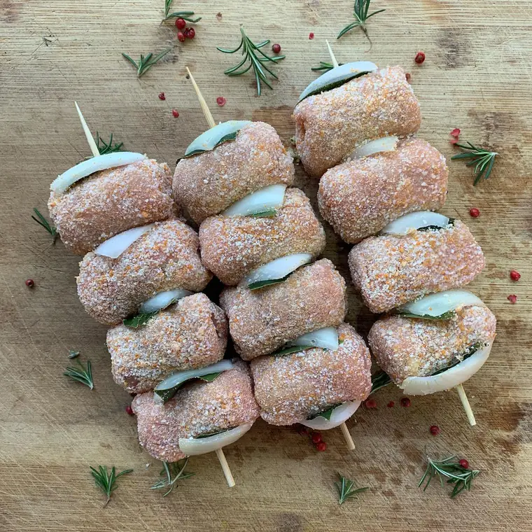 Spiedini di involtini impanati con cipolla e alloro, disposti su un tagliere di legno