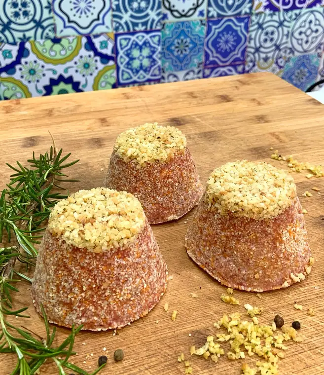 Tre preparazioni di carne a forma di cono con panatura e un ciuffo di pane aromatizzato in cima, su tagliere con rosmarino