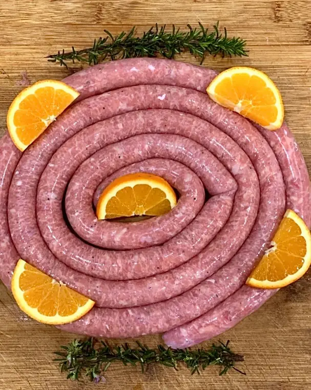 Salsiccia arrotolata a spirale con spicchi di arancia e rosmarino su un tagliere di legno
